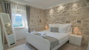 Ein Schlafzimmer mit Steinsturz, einem Bett mit weißer Bettwäsche, zwei Nachttischen mit Lampen und einem Fenster mit Vorhängen.