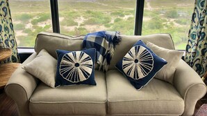 A sofa with two decorative pillows and a blanket, facing a large window with a view of the beach and ocean. - Seaview Oasis: Beachfront + Resort Access (Fernandina Beach)