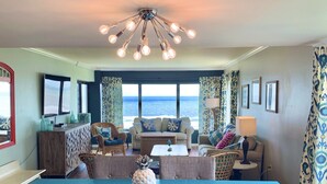 A spacious living room with a large table, comfortable seating, and a view of the ocean. - Seaview Oasis: Beachfront + Resort Access (Fernandina Beach)