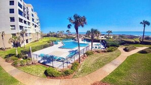 A hotel with a swimming pool, palm trees, and a view of the ocean. - Seaview Oasis: Beachfront + Resort Access (Fernandina Beach)