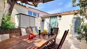 Ein Holztisch mit Stühlen, eine gelbe Tasse und eine Wasserflasche auf einer Terrasse mit Fliesenboden und einem Baum.