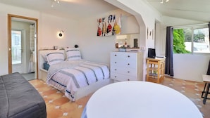 Ein Schlafzimmer mit Bett, Kommode, Schreibtisch und Stuhl. Ein Fenster bietet Blick auf Grünfläche.