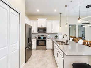 A modern kitchen with white cabinetry, stainless steel appliances, and a central island with a sink.