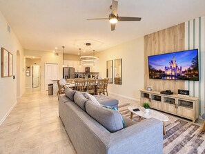 A modern living room with a sofa, TV, and a dining area in the background.