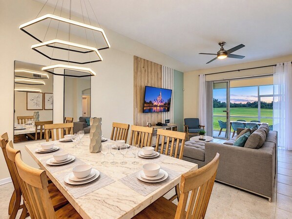 A modern dining area with a marble table, wooden chairs, and a television mounted on the wall.