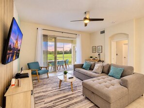 A modern living room with a flat-screen TV, a sofa, a coffee table, and a dining area with chairs.