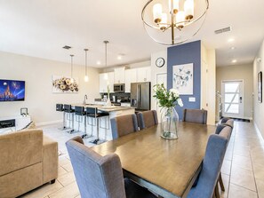 A modern kitchen with a central island, bar seating, and a dining area with a large table.