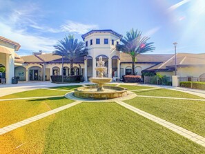A courtyard with a central fountain, surrounded by a well-maintained lawn and a building with arched doorways.
