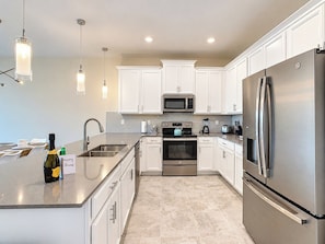 A modern kitchen with white cabinets, stainless steel appliances, a built-in oven, and a refrigerator.