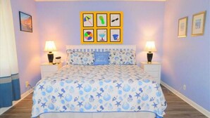 Un dormitorio con una cama, dos mesitas de noche y una pared decorada con seis cuadros.