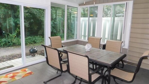 Un patio cubierto con una mesa, sillas, puertas correderas de vidrio grandes y un ventilador de techo.