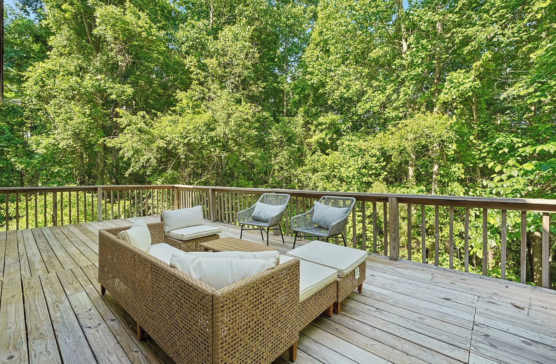 A deck with wicker furniture and a table, surrounded by a wooden railing.