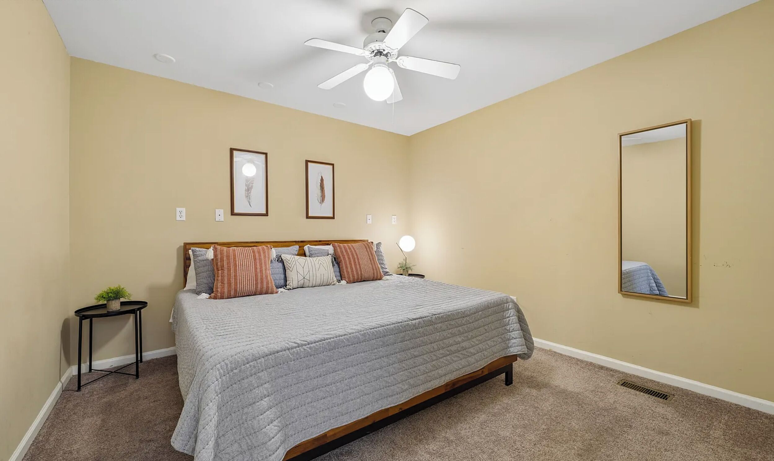 Une chambre à coucher comprenant un lit, un ventilateur de plafond, une table de chevet avec une lampe et un miroir fixé au mur.
