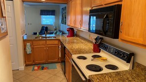 A compact kitchen with wooden cabinets, a white stove, and a black microwave.