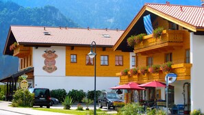Un edificio alpino tradicional con techo de tejas rojas, balcones de madera con jardineras de flores y un letrero que indica un restaurante local.