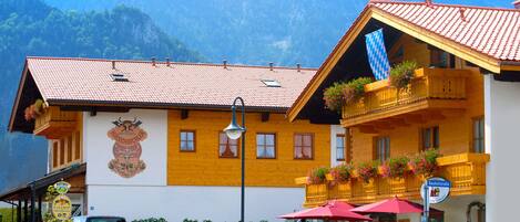 Ein traditionelles Gebäude in den Alpen mit roten Ziegeldach, Holzbalkonen mit Blumenkästen und einem Schild, das ein Lokal ausweist.