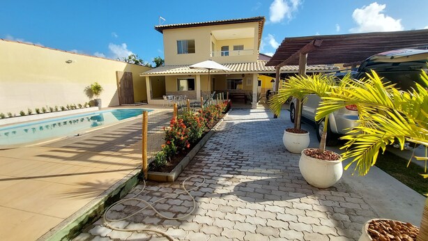 Uma área à beira da piscina com um caminho de azulejos, uma piscina e plantas em vasos.
