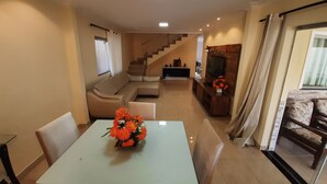 Uma sala de estar moderna com um sofá, uma mesa de jantar com cadeiras, uma televisão e uma escada que leva a outro andar.