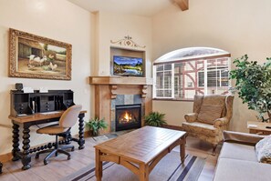 A living room with a fireplace, a television, a desk with a computer, and a comfortable seating area.