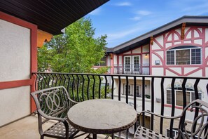 Un balcon doté d’une table ronde et de deux chaises, offrant une vue sur un immeuble au style architectural particulier.
