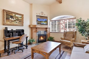 A living room with a fireplace, a television, a desk with a computer, and a comfortable seating area.