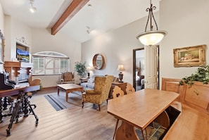 A spacious living room with a wooden dining table, comfortable seating, a large mirror, and a television.