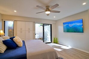 Un dormitorio con una cama, ventilador de techo, un cuadro y puerta corrediza de vidrio que da a un patio.