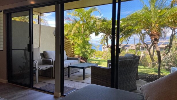 Ein Zimmer mit einer Glasschiebetür, die auf eine Terrasse mit Gartenmöbeln und Palmen führt.