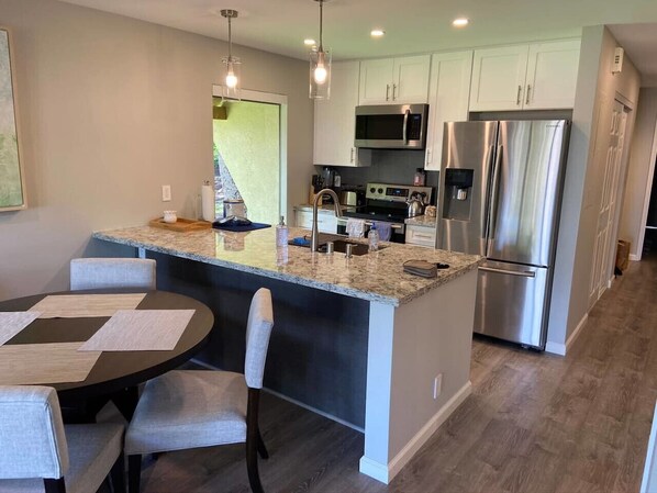 A modern kitchen with granite countertops, stainless steel appliances, and a dining area with a round table and chairs. - Front row of Maui Kamaole. Newly renovated unit wi (Kihei)
