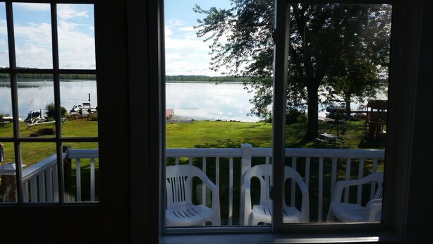 Blick aus einem Zimmer mit großem Fenster auf eine Wiese mit einem See, einem Steg und einem Spielplatz.