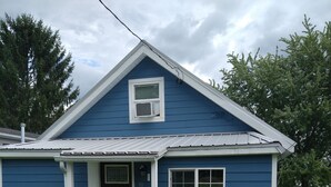 Ein eingeschossiges Haus mit Satteldach, einer Veranda und einem kleinen Fenster.