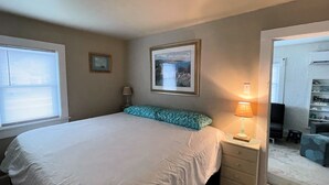 Un dormitorio con cama, mesita de noche, lámpara y un cuadro en la pared.