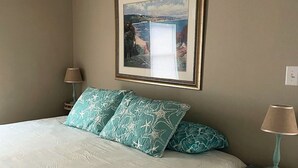 A bedroom with a bed, two nightstands, a framed picture on the wall, and a lamp on one nightstand.