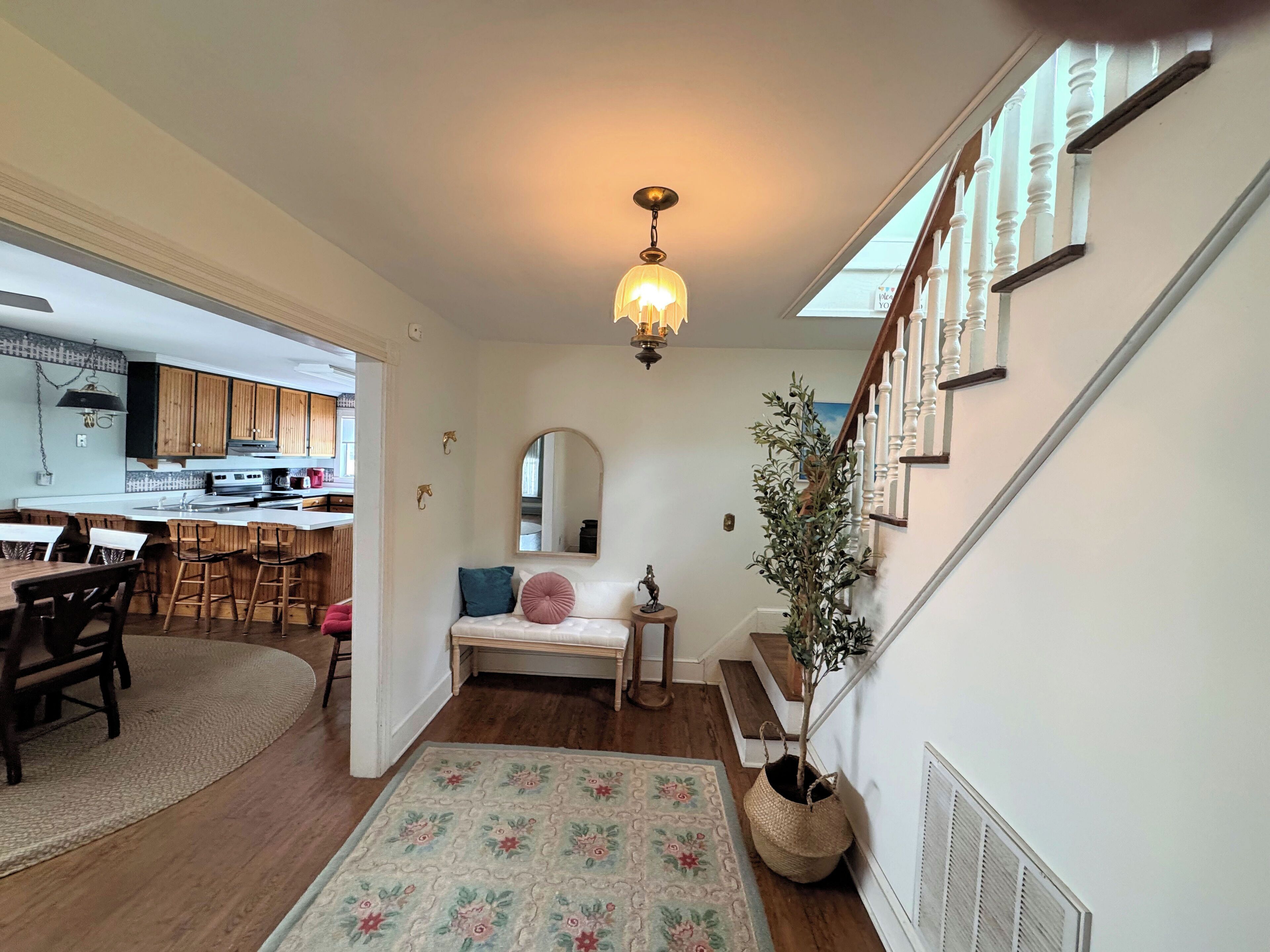 Un intérieur de maison comprenant un coin repas, une cuisine, un escalier et un salon avec un tapis et une plante en pot.