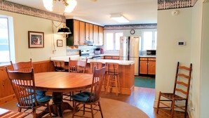 A kitchen with wooden cabinets, a dining table with chairs, and a refrigerator. - Miss Agnes - Water Front 3BR home PET FRIENDLY, NO LINENS PROVIDED (Chincoteague)