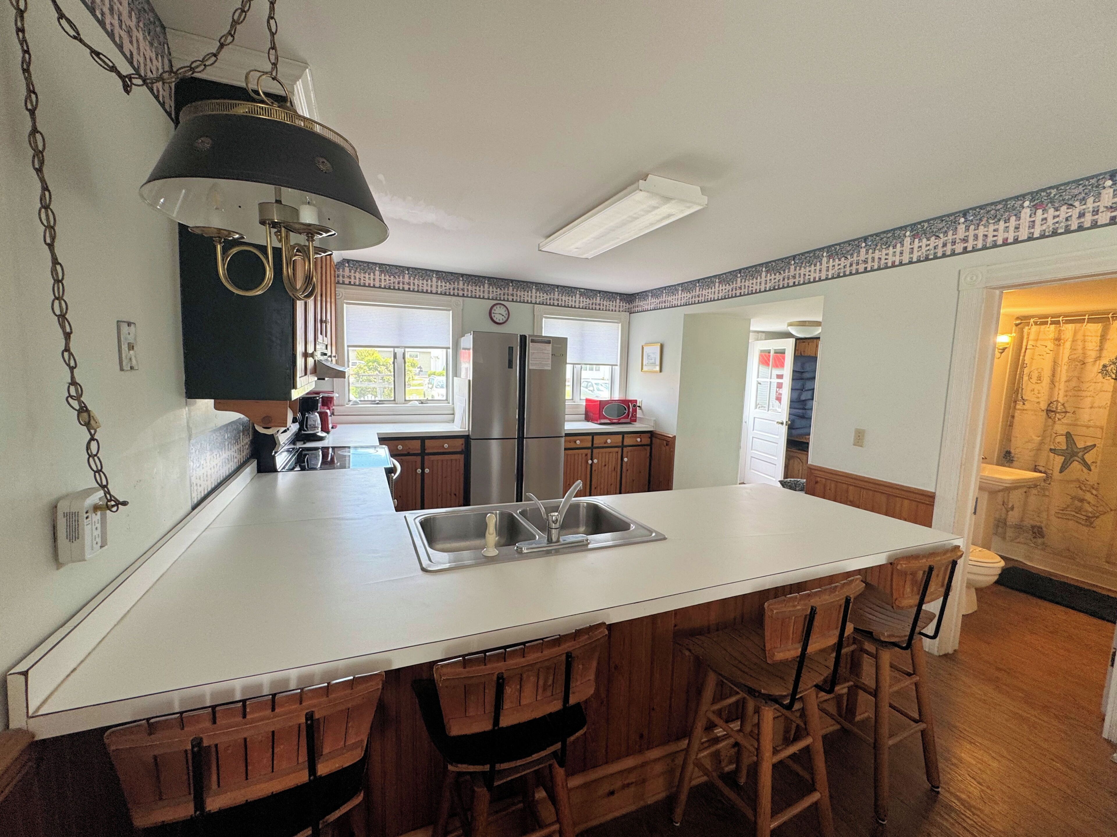 Une cuisine dotée d’un îlot central, de tabourets de bar en bois, d’un réfrigérateur et d’un four à micro-ondes.