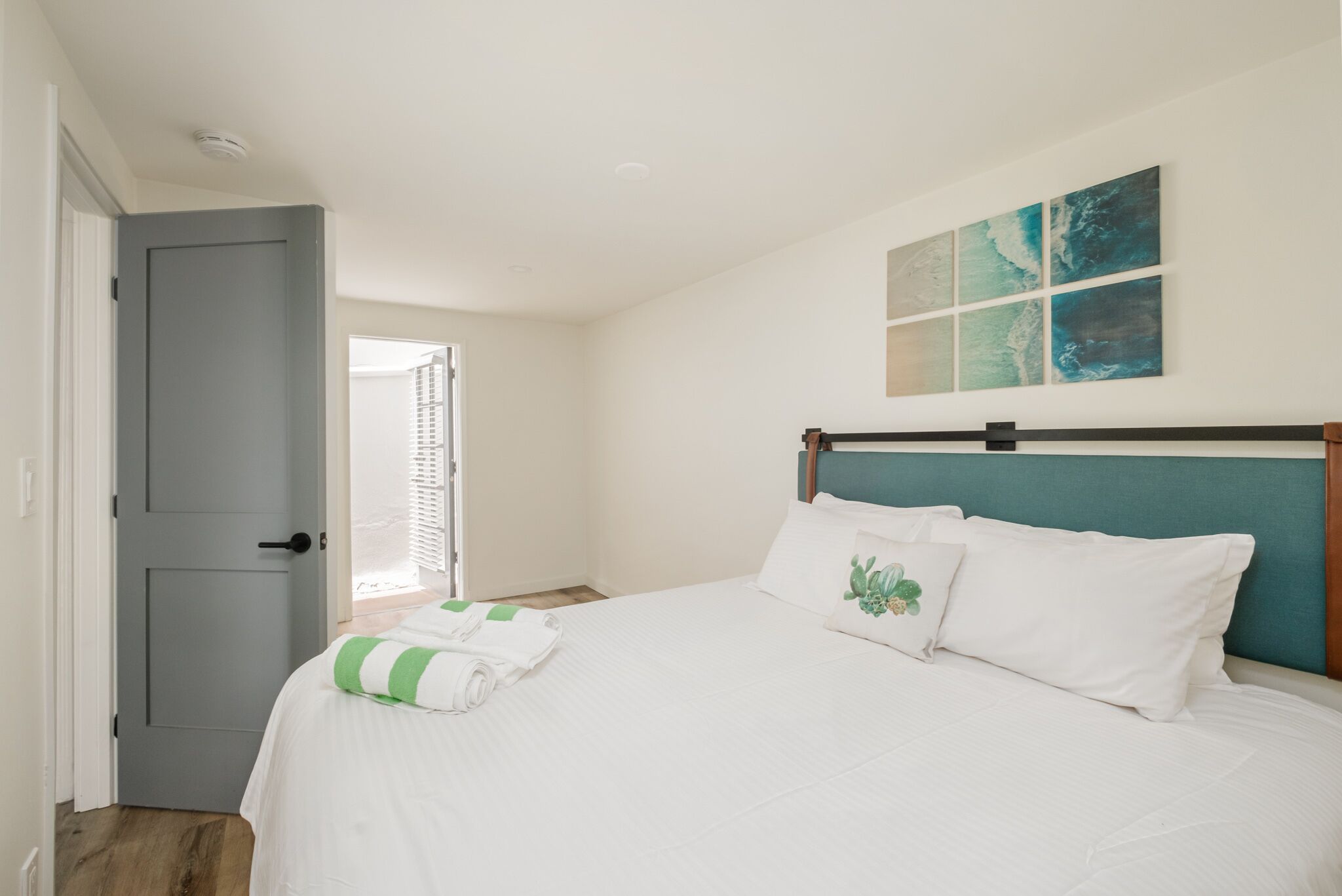 A bedroom with a bed, a grey door, and a window with blinds.