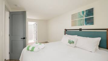A bedroom with a bed, a grey door, and a window with blinds.