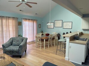 Ein Wohnzimmer mit gepolstertem Sofa, ein Essbereich mit Holztisch und Stühlen, eine Küche mit Spüle und Arbeitsplatte sowie ein Deckenventilator.
