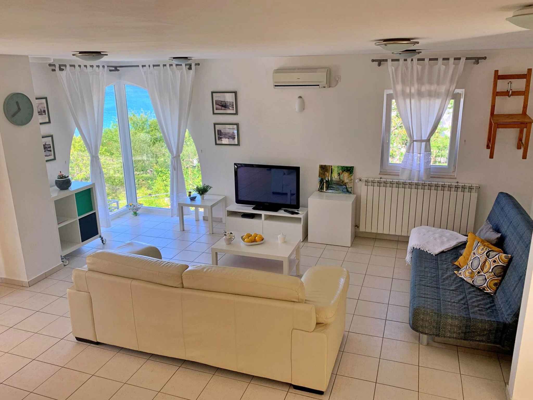 Un salon avec un canapé, un téléviseur, une petite table sur laquelle se trouvent des fruits et un divan bleu.