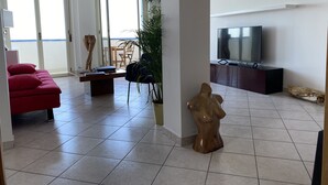 A living room with a red sofa, a wooden sculpture, a TV on a stand, and a view of the outside through large windows. - --SunRise-- (Montesilvano)