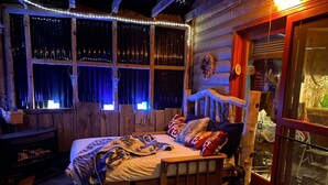 Una habitación rústica con una cama de madera, un sillón mecedora y una ventana con cortinas.
