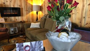 Una sala de estar acogedora con una pared de madera, un televisor de pantalla plana, un sofá, un jarrón de vidrio con rosas rojas y un balde con hielo y una botella de cerveza Korbel.