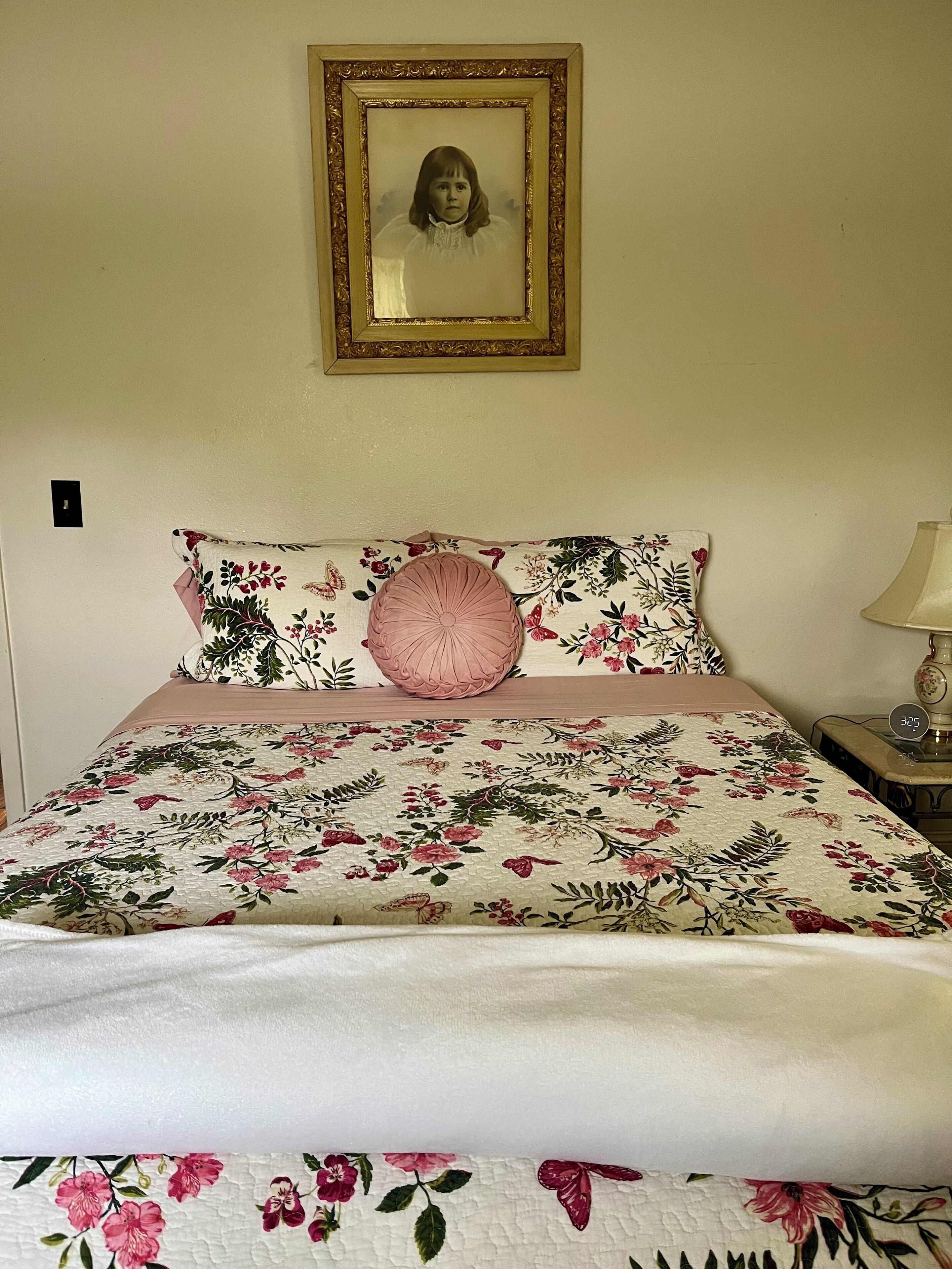 A bed with floral bedding, a framed picture above, and a bedside lamp.