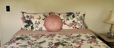 A bed with floral bedding, a framed picture above, and a bedside lamp.