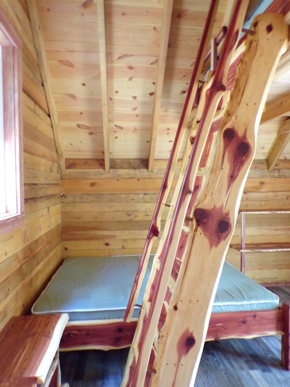 A wooden cabin interior with a bed, a window, and a wooden ladder. - Shady Pine Primitive Cabin 2 @Spring Lake Ranch (Potosi)