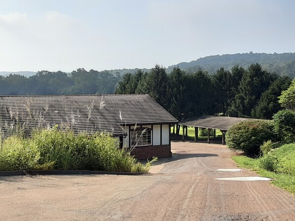 A rural building with a dirt road leading to it, surrounded by greenery and hills.