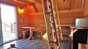 A wooden cabin interior with a ladder, a table, and a microwave. - Shady Pine Primitive Cabin 2 @Spring Lake Ranch (Potosi)