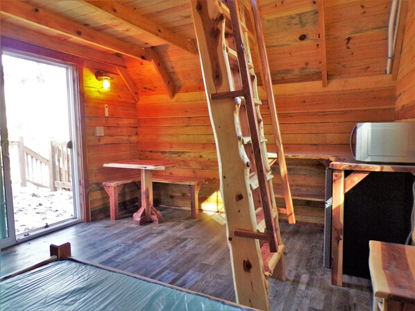 A wooden cabin interior with a ladder, a table, and a microwave. - Shady Pine Primitive Cabin 2 @Spring Lake Ranch (Potosi)