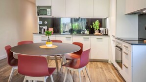 Cocina moderna con armarios blancos, microondas y comedor con mesa redonda y sillas rojas.